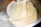 A person is pouring thick, creamy white liquid from one container into another stainless steel container.