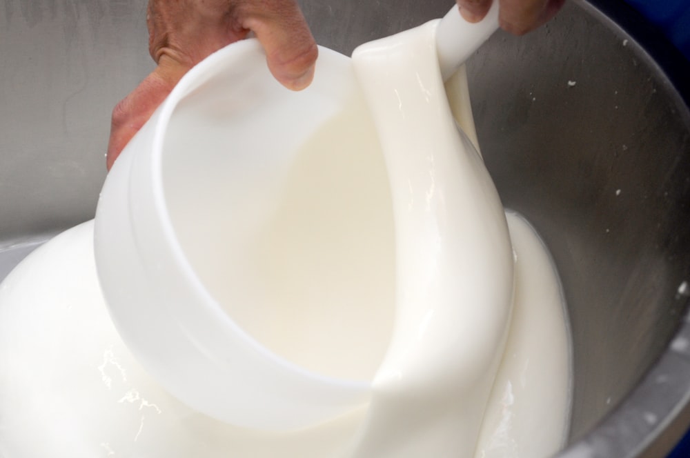 a person pouring milk into a metal bowl