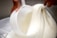 A close-up view of a white, creamy substance being poured and mixed with a large scoop in a smooth, flowing manner. The hands of a person are visible, holding the scoop and managing the thick texture.