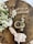 A wooden table with a rustic aesthetic hosts a small arrangement of white flowers in a white vase, a cup of coffee, a neatly folded napkin with a white floral decoration, and a decorative sign that spells 'Home' in metallic letters.
