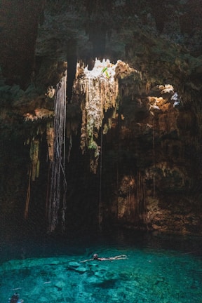 Close-up of a turquoise cenote with a cyclist preparing to dive in, surrounded by tropical plants