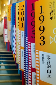 Brightly colored banners with large printed years and Chinese text line a staircase. Each banner features a filmstrip design on the side and contains numbers such as 1993 and 2001, alongside additional text and graphical elements. The perspective creates a visually striking effect as the banners follow the angle of the stairs.