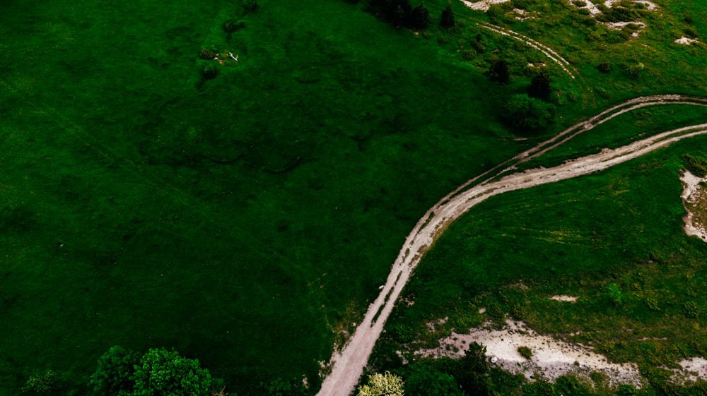 an aerial view of a dirt road in the middle of a green field