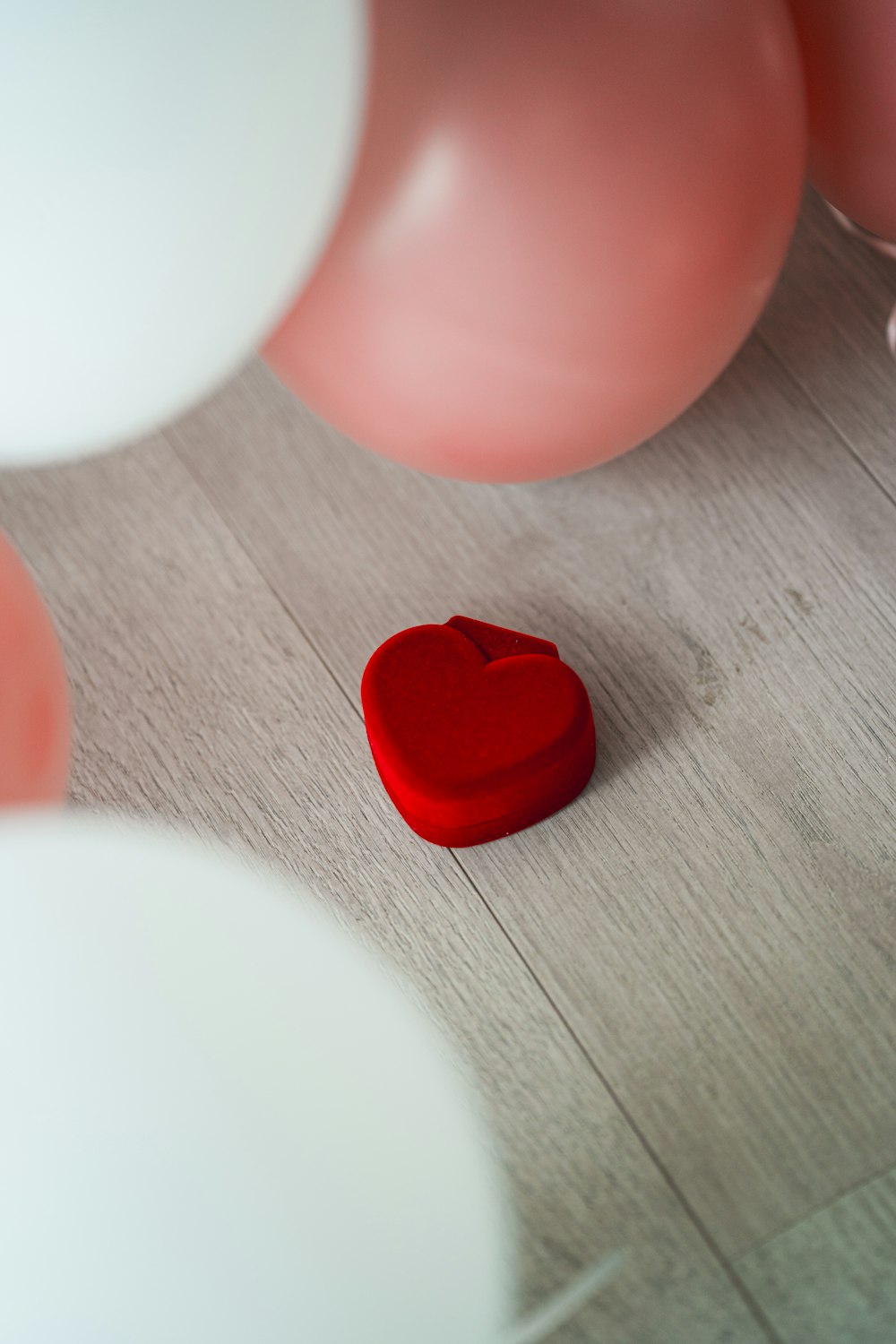 a red heart sitting on the floor surrounded by balloons