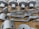 A collection of metallic, machined components neatly arranged on a cardboard surface. The parts vary in shape and size, including cylindrical and flat pieces with holes and grooves. Some parts have the letters 'DRG' etched into them.