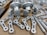 A collection of metallic machine parts arranged on a cardboard surface. The parts include connectors, rods, and brackets, all of which appear to be made of silver-colored metal. The components are neatly laid out, showcasing various shapes and sizes, with some parts having holes for assembly purposes.