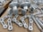 A collection of metallic machine parts arranged on a cardboard surface. The parts include connectors, rods, and brackets, all of which appear to be made of silver-colored metal. The components are neatly laid out, showcasing various shapes and sizes, with some parts having holes for assembly purposes.