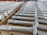 A neatly arranged collection of large metal bolts with hexagonal heads and threaded bodies, aligned in multiple rows on a wooden pallet, suggesting an orderly industrial setting.