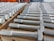 A neatly arranged collection of large metal bolts with hexagonal heads and threaded bodies, aligned in multiple rows on a wooden pallet, suggesting an orderly industrial setting.