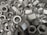 A pile of metallic hex nuts overlapping each other, showcasing their threaded interiors and outer hexagonal shape.