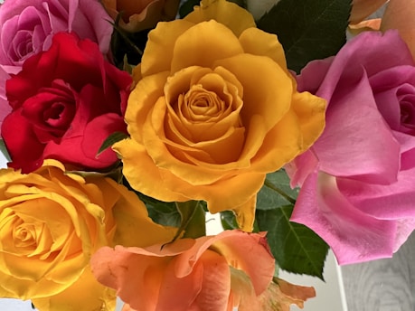 A close-up of a colorful mixed bouquet featuring roses, lilies, and greenery wrapped in rustic paper.