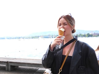 A smiling customer enjoying a kiwi cone at a sunny outdoor market.