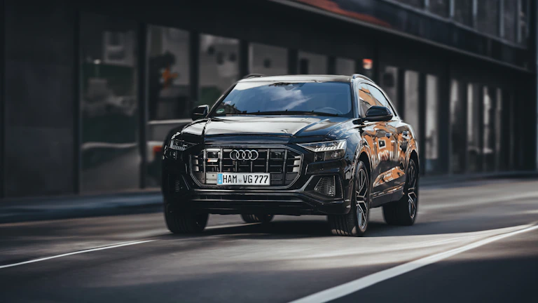 Black luxury SUV cruising down a city street lined with modern skyscrapers.