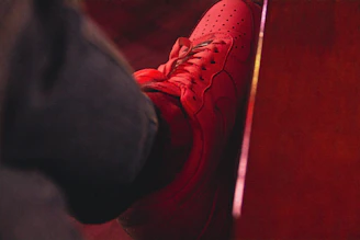 Close-up of a vibrant red high-top sneaker with detailed stitching on a wooden floor.