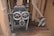 An old industrial machine with large metal gears and pulleys is positioned on a wooden floor. The machine's components appear worn and rusty, surrounded by a wooden structure with beams and panels.