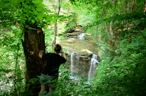 A candid moment of a traveler capturing a photo of a majestic waterfall surrounded by lush greenery.