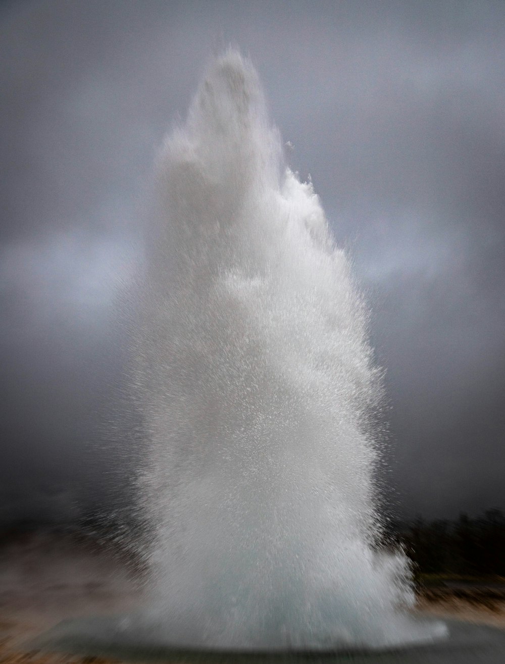 a large wave hitting into the ocean on a cloudy day