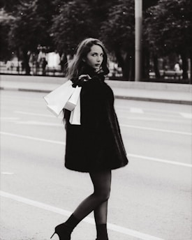 A stylish young woman in a trendy outfit posing with shopping bags on a city street.