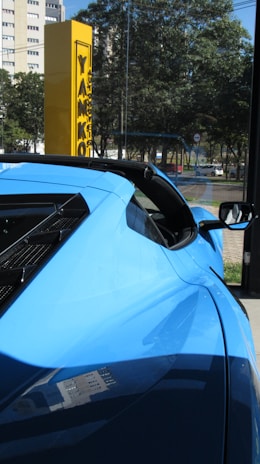 Close-up of a sleek blue rental car with shiny orange accents parked by a family-friendly park.