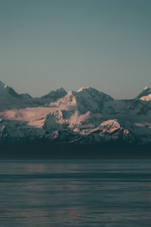 Snow-capped mountains reflected in a serene alpine lake during golden hour.