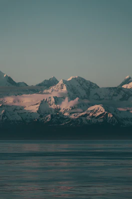 Snow-capped mountains reflecting in a still alpine lake at dusk.