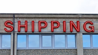 A concrete building facade displays the word 'SHIPPING' in bold, red neon letters above a series of uniform, rectangular windows with reflective glass.