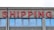 A concrete building facade displays the word 'SHIPPING' in bold, red neon letters above a series of uniform, rectangular windows with reflective glass.