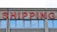 A concrete building facade displays the word 'SHIPPING' in bold, red neon letters above a series of uniform, rectangular windows with reflective glass.