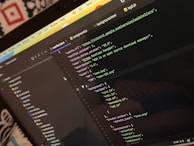 A computer screen displays a code editor with a dark theme. The code is related to a manifest file, showing JSON format data, including URLs, version numbers, and a description of an 'Xtreme Download Manager'. There are also multiple tabs open with filenames like 'background.html' and 'bg2.js'.