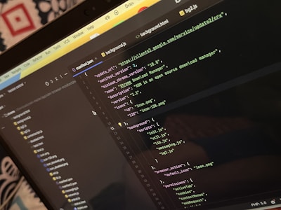 A computer screen displays a code editor with a dark theme. The code is related to a manifest file, showing JSON format data, including URLs, version numbers, and a description of an 'Xtreme Download Manager'. There are also multiple tabs open with filenames like 'background.html' and 'bg2.js'.