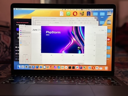 A laptop displaying a calendar application with the month of June 2023 open. The PhpStorm application is prominently visible in one of the tabs. The desktop is cluttered with various icons and folders. The background has a gradient wallpaper and the taskbar shows several application icons.