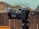 A professional camera is mounted on a tripod outdoors, with a blurred background of wooden fencing and rooftops. The camera features a large lens with detailed branding visible and several dials and buttons.