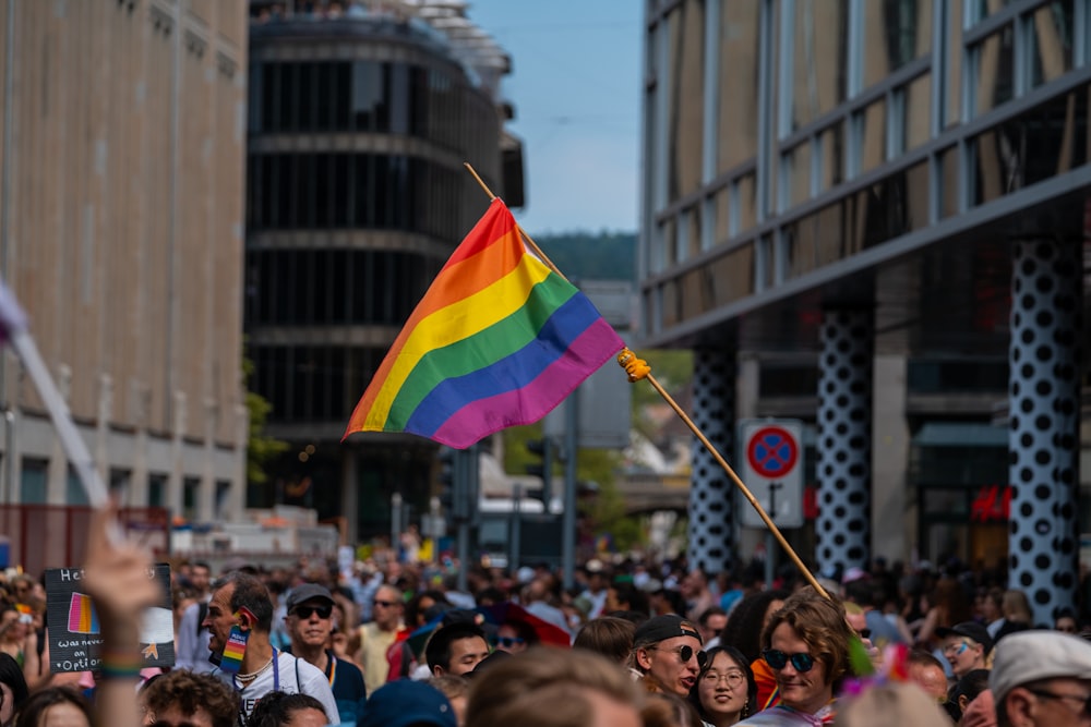 a crowd of people walking down a street holding a rainbow flag