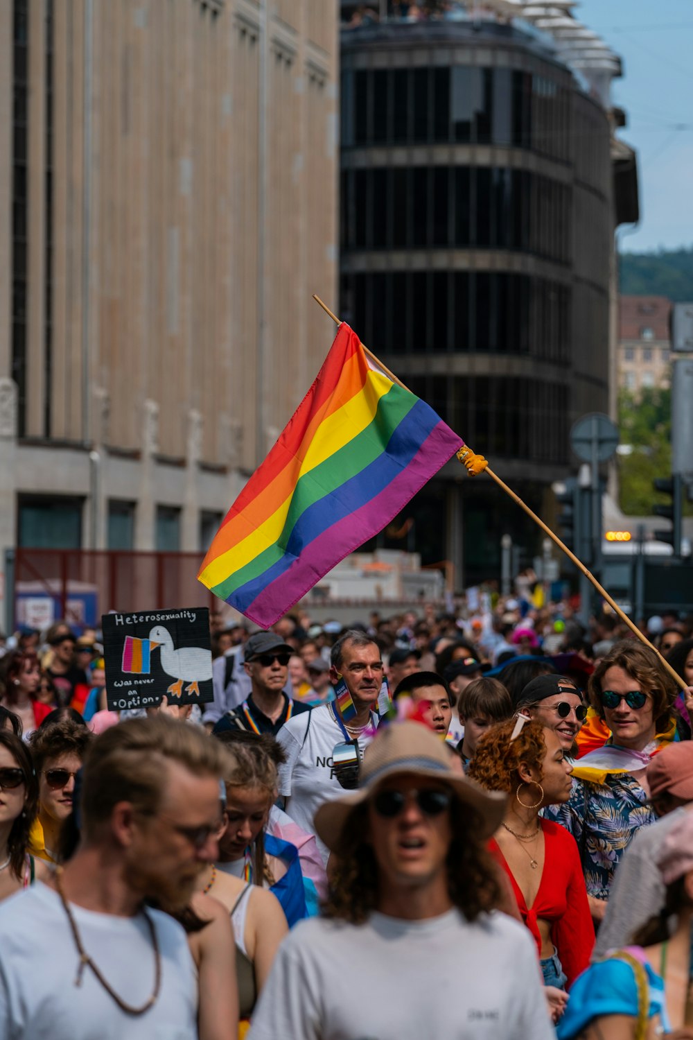 a crowd of people walking down a street holding a rainbow flag
