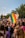 A vibrant crowd gathers at an outdoor event, with numerous individuals in colorful attire and some holding rainbow flags. A prominently displayed sign reads, 'I'M NOT AS GAY AS I LOOK (I'M MUCH GAYER)'. The setting is bright with clear skies, suggesting a festive and inclusive atmosphere.