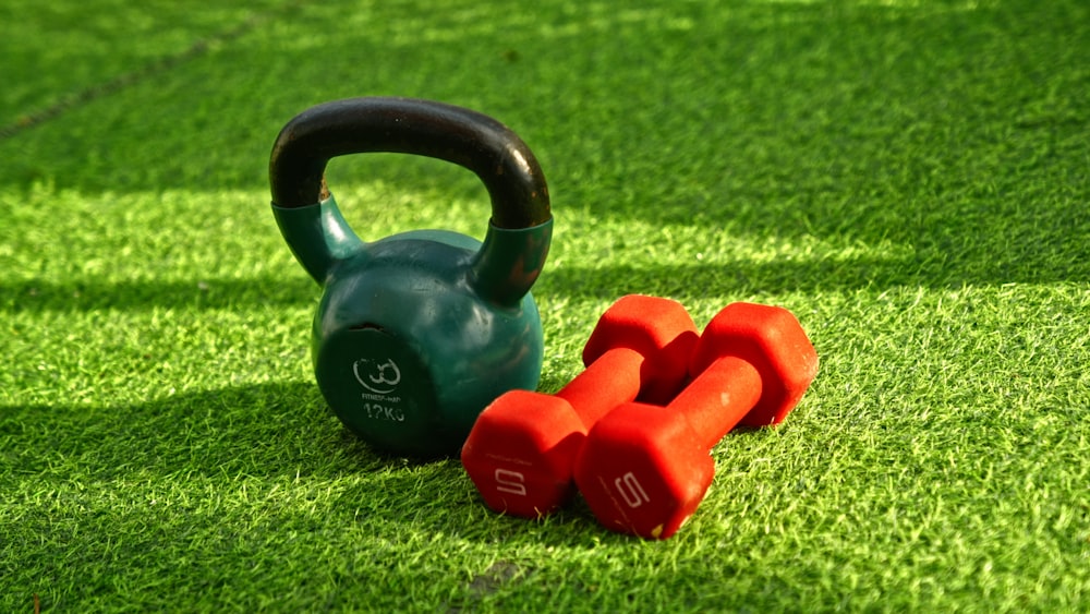 a kettle and two red dumbs on a green field