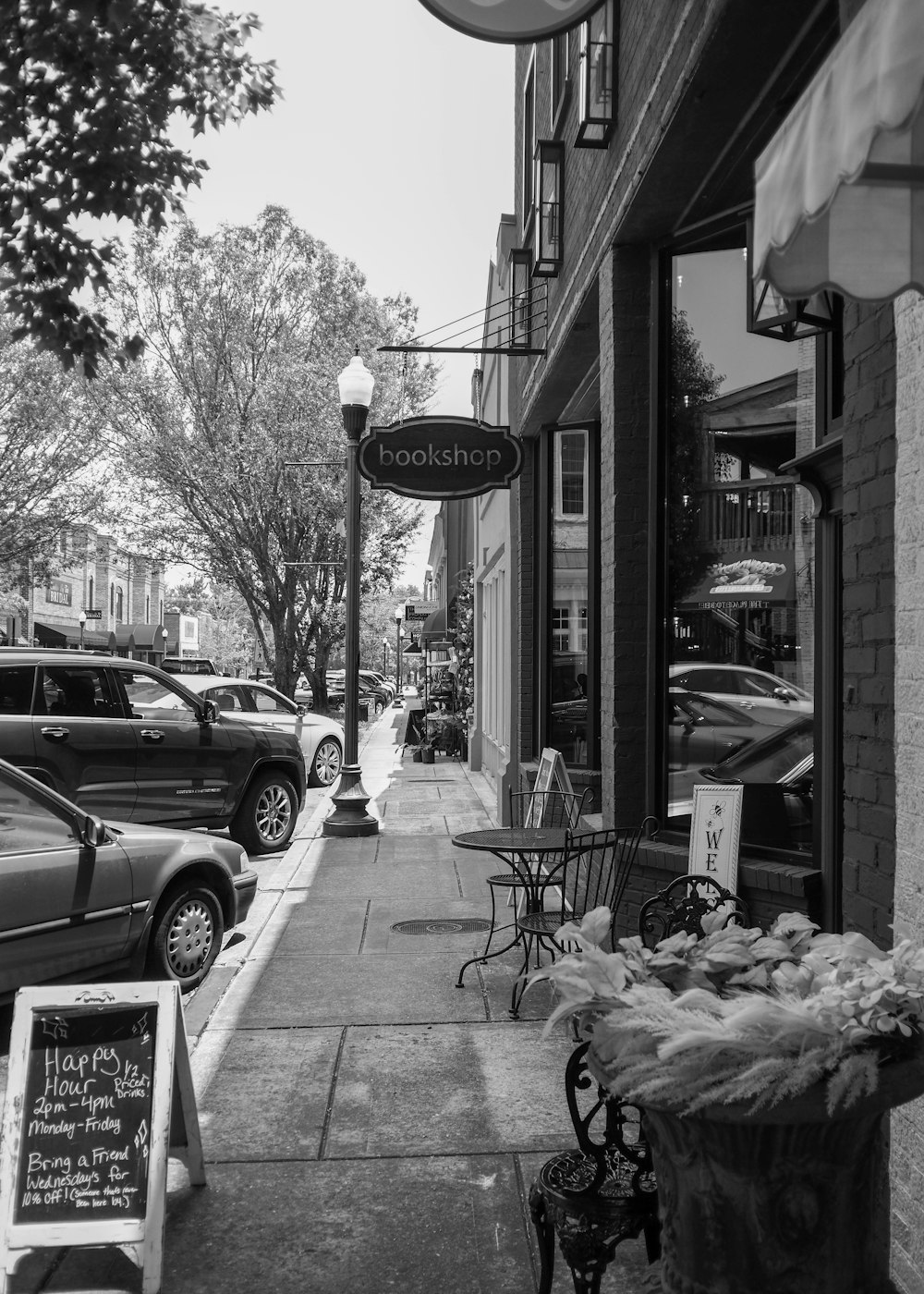 a black and white photo of a sidewalk with parked cars