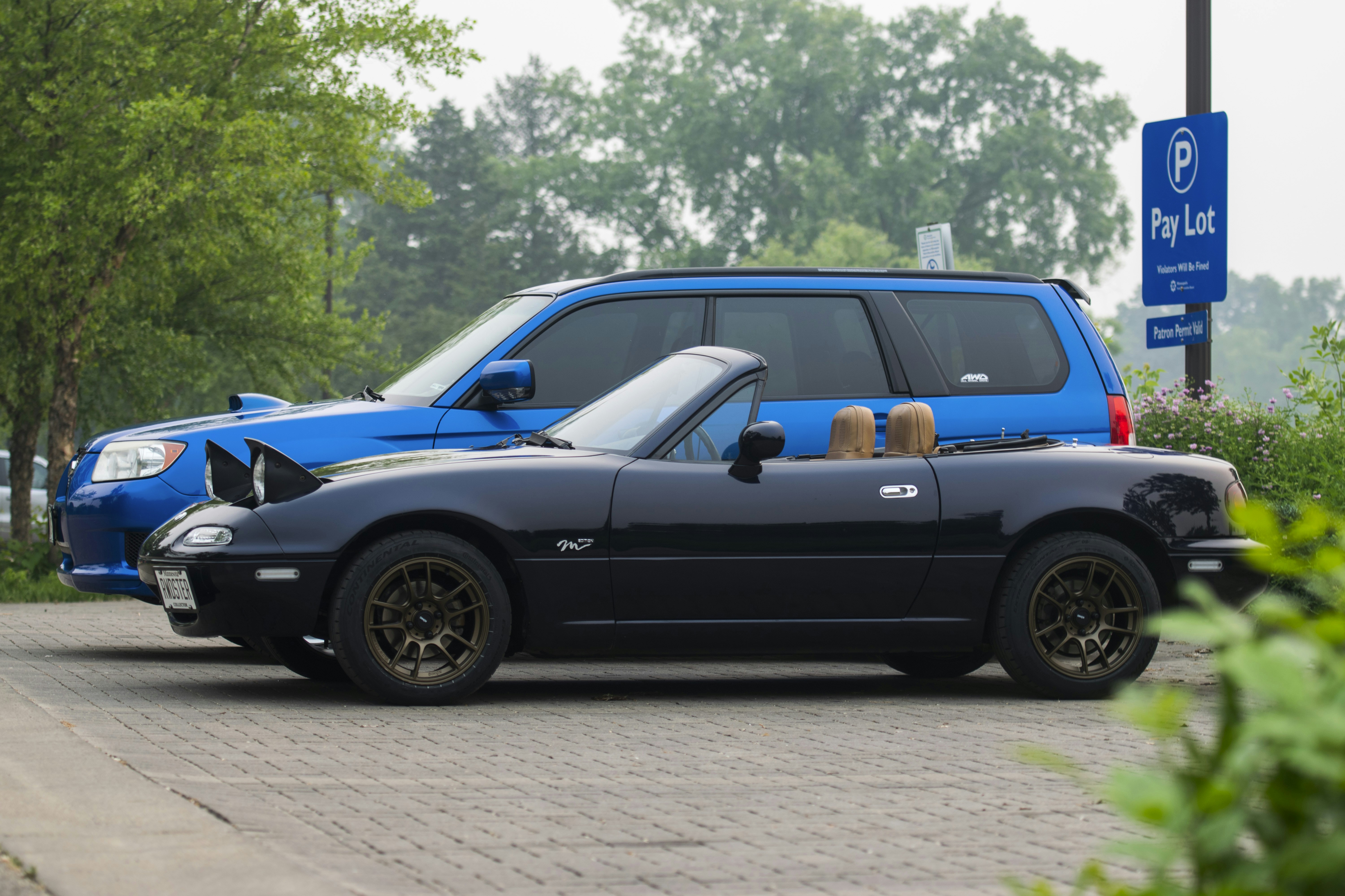 a blue car with a dog in the hood parked next to a blue car