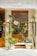 A storefront decorated with green plants in various pots and hanging containers. The window is framed with wooden accents and features a person inside, arranging flowers. The facade includes a decorative snail motif.