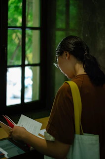 A candid shot of Ana Carolina Alves reviewing documents by a window with natural light.