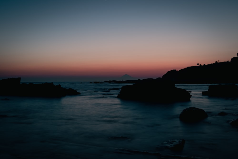 the sun is setting over the ocean with rocks in the foreground