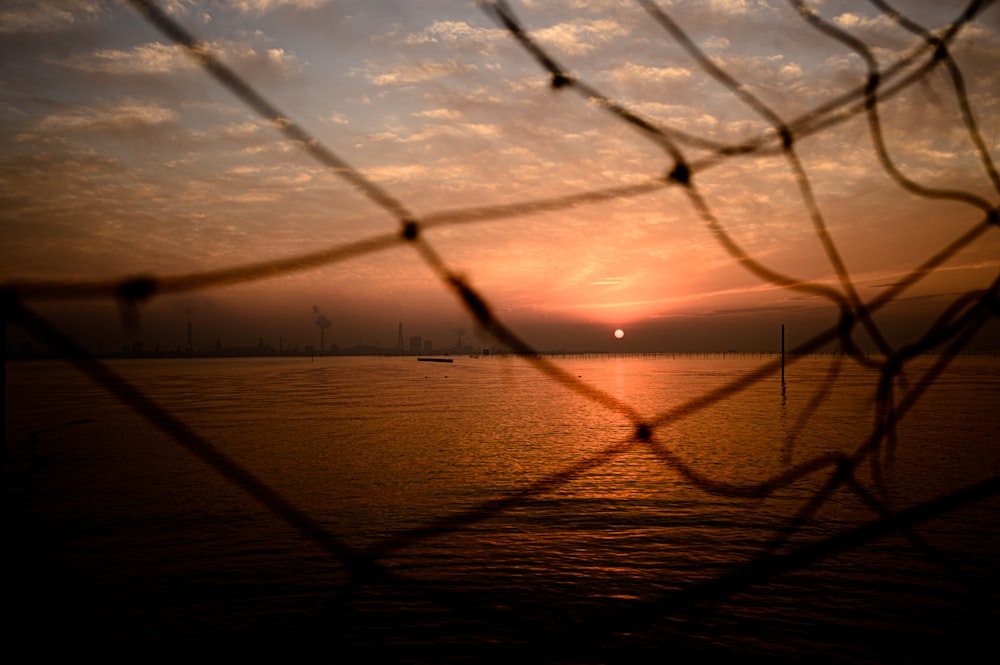 uma vista de um pôr do sol através de uma cerca