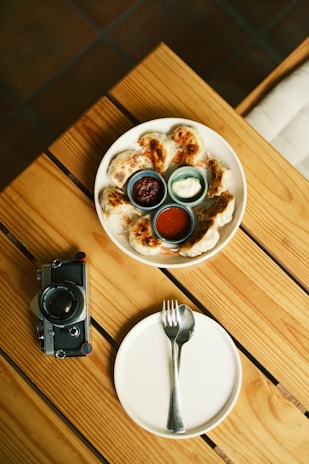 A rustic wooden table set with homemade gyoza dumplings arranged on a ceramic plate.
