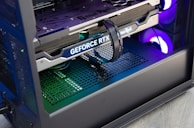A close-up view of the interior of a computer casing showcasing a high-end graphics card with 'GeForce RTX' branding. The graphics card is secured in its slot, and several power cables are attached. The background reveals cooling fans illuminated with RGB lighting.