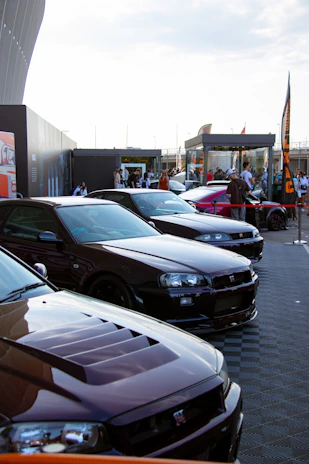 A lineup of sleek sports cars parked side by side with food trucks and people enjoying live music in the background.