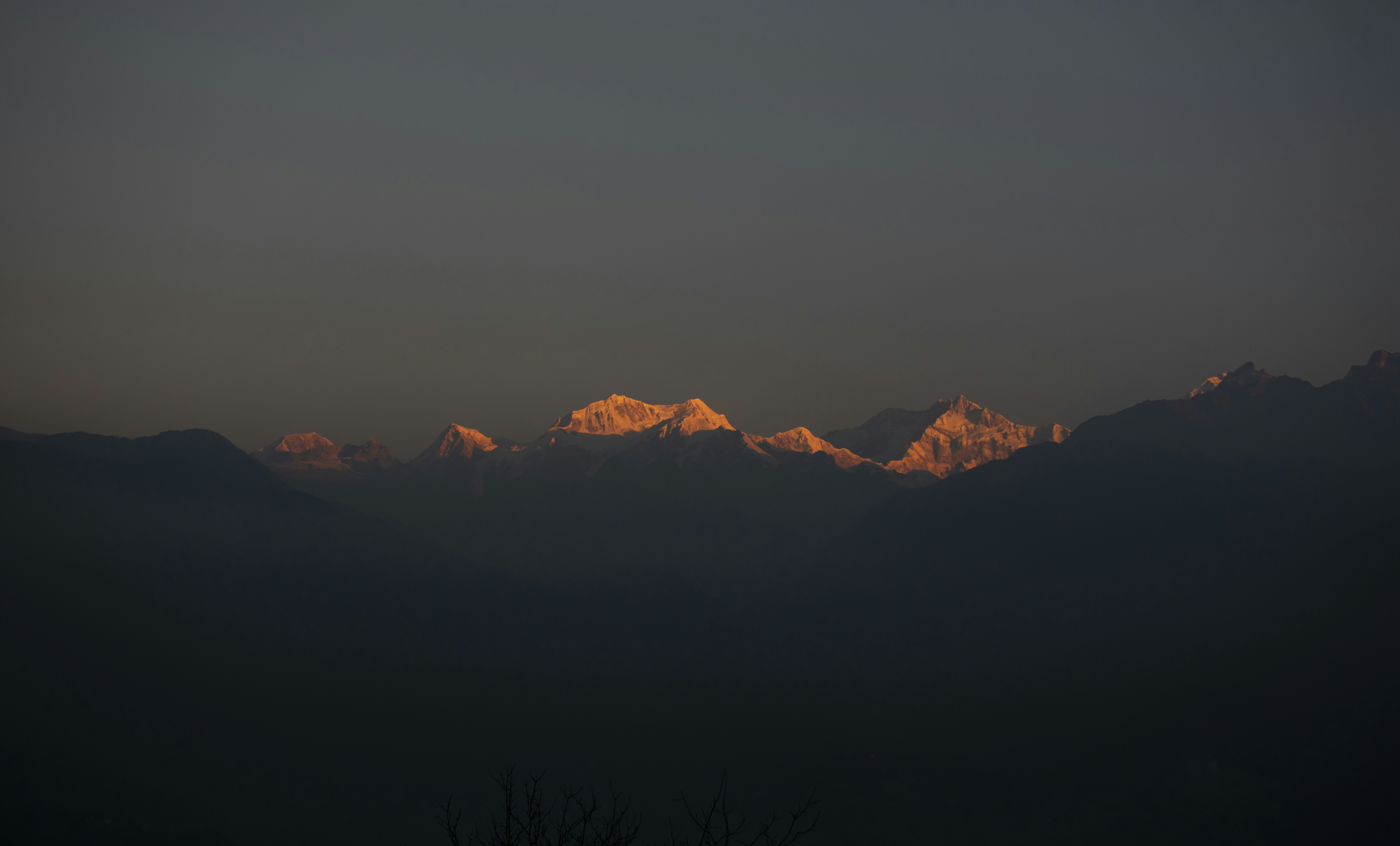 First sunlight turning the summits of the Kanchenjunga range gold above the dark ridges of West Sikkim, seen from Pelling at dawn