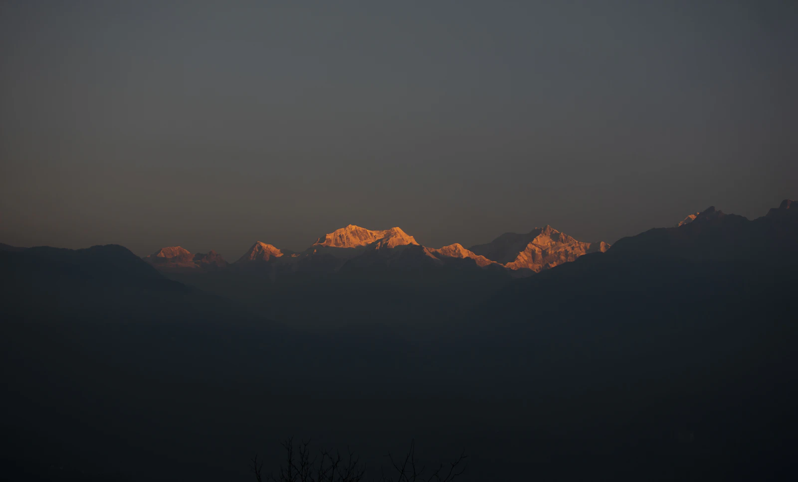 First sunlight turning the summits of the Kanchenjunga range gold above the dark ridges of West Sikkim, seen from Pelling at dawn