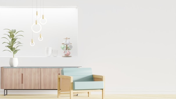 A minimalist interior design featuring a wooden sideboard with sleek lines and a potted plant on top. Modern pendant lights with circular designs hang from the ceiling, and decorative items are arranged on a recessed shelf. A light blue armchair with a wooden frame is positioned in the foreground, enhancing the contemporary aesthetic.