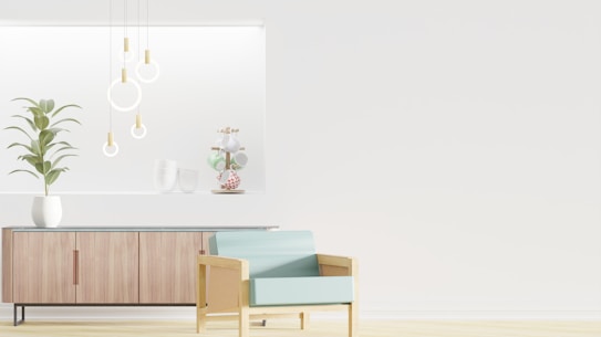 A minimalist interior design featuring a wooden sideboard with sleek lines and a potted plant on top. Modern pendant lights with circular designs hang from the ceiling, and decorative items are arranged on a recessed shelf. A light blue armchair with a wooden frame is positioned in the foreground, enhancing the contemporary aesthetic.