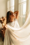 A serene shot of a woman in a clean, logo-free premium solid color top, standing by a sunlit window.